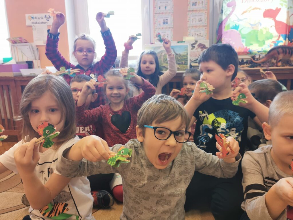 Dzieci prezentują swoje prace papierowe dinozaury na klamerkach.