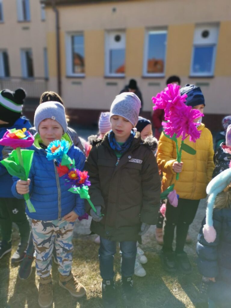 Dzieci stoją z kolorowymi kwiatami.